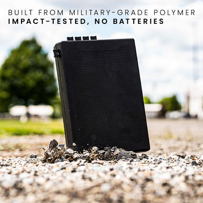 STOPBOX PRO in black, made from military-grade polymer, shown on gravel with a blurred background of trees and buildings.
