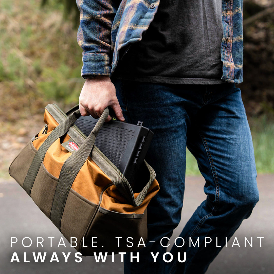 STOPBOX PRO in a tan and green bag, held by a person wearing a plaid shirt and jeans, outdoors on a path.